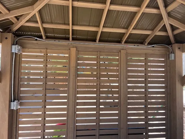 A wooden pergola wired for a fan and string lights