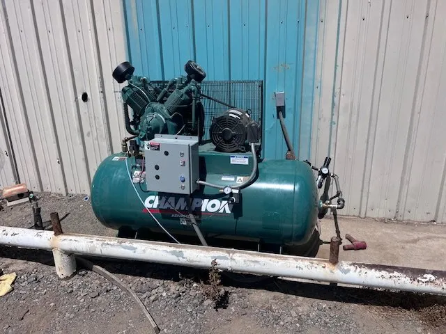 Green three-phase air compressor outside a metal shop building